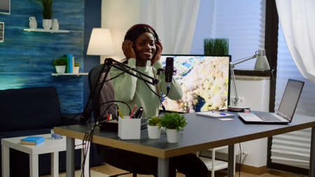 African blogger influencer putting on headset and smiling before recording video blog, looking at...