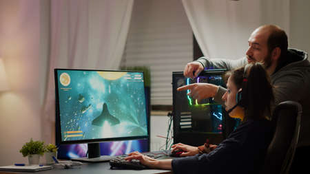 Man gamer teaching his girlfriend playing space shooter video game on RGB powerful personal...