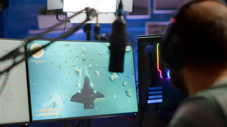 Close-up of streamer man talking at microphone with other players during space shooter tournament. Online streaming cyber performing video games competition using technology network wirelessの写真素材