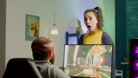 Nervous woman screaming at husband while he is playing space shooter videogame on RGB powerful...