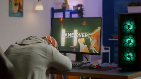 Game over for sad gamer playing shooter video games on powerful computer using RGB keyboard in...