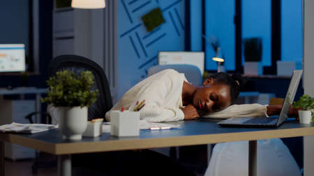 Exhausted overload african business woman falling asleep on desk with open laptop monitor while...