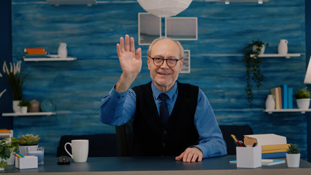 POV of elderly aged man waving during a video conference with business partners working from home....