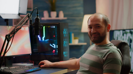 Streamer man looking at camera smiling while streaming videogames using stream chat. Pro cyber...