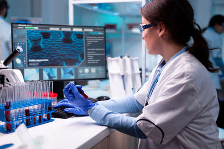 Scientist typing on laptop holding vacutainer blood healthcare chemistry. Researcher in chemical medicine lab working with professional technology equipment for healthcare development.の写真素材