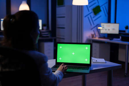 Back view of business woman looking at green screen laptop sitting at desk in start up company...