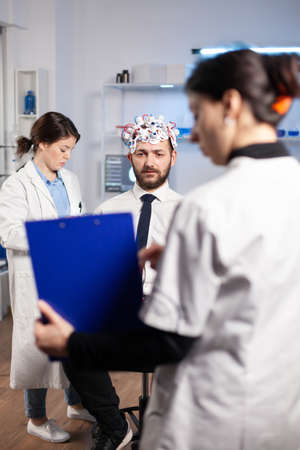 Researcher neurologist doctor asking mans illness symptoms looking at clipboard before brain scan...