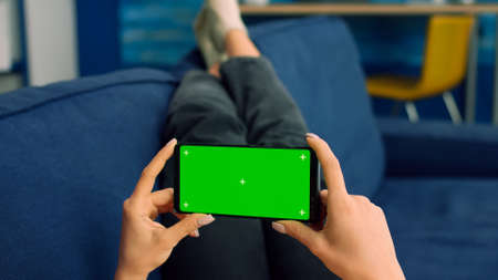Business woman lying on sofa holding isolated phone with mock up green screen chroma key during...