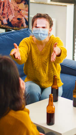 Funny friends with sticky notes on foreheads enjoying name game gesturing during new normal party...
