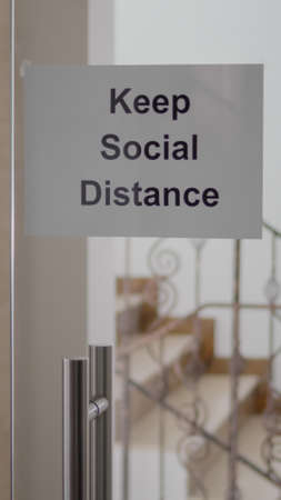 Glass office dor with keep social distance poster on it, modern office stairs duting  pandemic,...