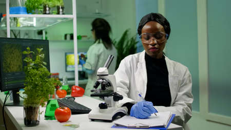 Biologist researcher scientist looking at leaf sample under medical microscope while writing...