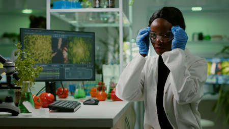African scientific woman putting her medical glasses looking at camera while her collegue analyzing scientific expertise. Specialists team researching genetic mutation developing dna GMO biology testの写真素材
