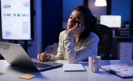 Exhausted freelancer falling asleep in front of laptop checking financial reports in company office...