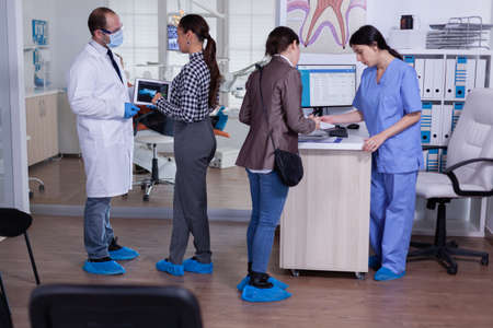 Orthodontist using tablet explaining dental x ray to patient standing in waiting area of...