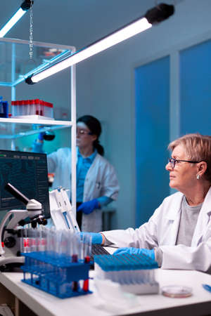 Senior doctor in white coat working on computer, vaccine, chemistry, test tube, medicine. Doctor...