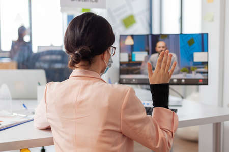 Woman discussing job project with business man during remote video call in new normal office in time...