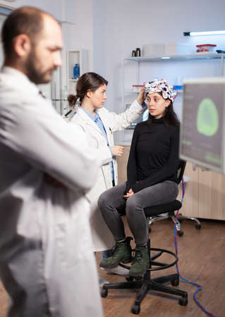 Neuroscience scientist adjusting headset with sensors on womna patient in modern lab during brain scanning. Nervous system analysis, clinic equipment. Doctor brain scan.の写真素材