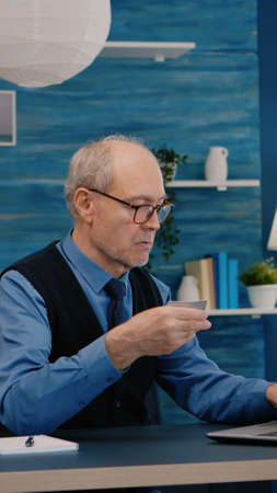 Retired man making online payment using credit card on laptop working from home. Senior person...