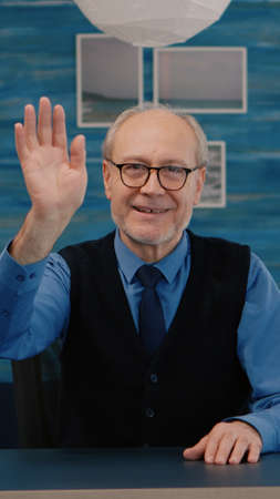 POV of elderly aged man waving during a video conference with business partners working from home....