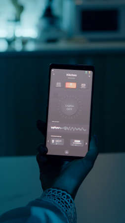 Woman sitting in house with automation light system holding smartphone turning on light using voice...