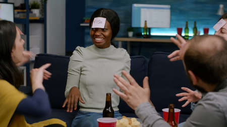 Group of friends with sticky notes playing guess who game drinking beer during home party.