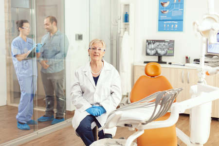 Portrait of senior dentist woman sitting on chair in stomatological hospital office.の写真素材