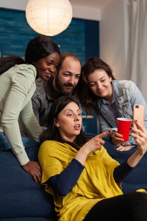Multiracial friends hanging out late at night watching funny entertainment video on smartphone.の写真素材