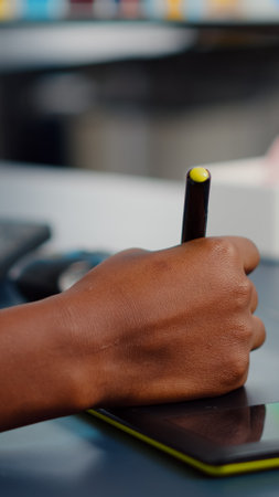 Close up on hand of african photo editor drawing on graphic tablet editing customer photo on computer with two monitors.の写真素材