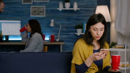Confident woman reading email notification using smartphone while relaxing on sofa late at night in...