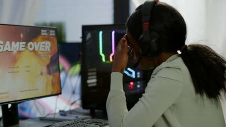 Furious african woman gamer with headset losing space shooter video game with graphics during gaming...