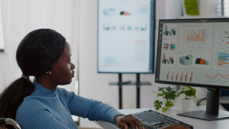 Black disabled handicapped businesswoman immobilized in wheelchair working at financial project typing on computer showing data prosessing on display sitting in start up business officeの写真素材
