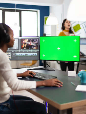 Black videographer using computer with chroma key, mock up isolated display editing video and audio footage. Woman editor processing film montage on green screen working in digital multimedia companyの写真素材