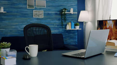 Pretty simple modern decor of cozy apartment with no people in it and television in background. Empty workspace of freelancer worker with laptop computer on desk and cup of coffee.の写真素材
