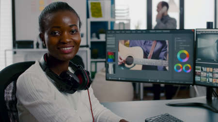 Close up of african video editor turning head at camera looking and smiling working in start up creative agency office. Black videographer editing video project using post production softwareの写真素材