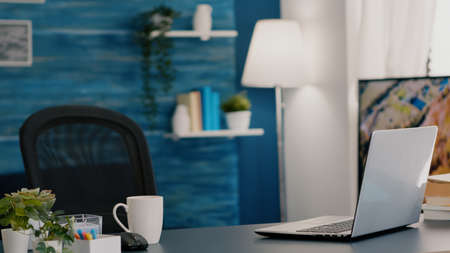 Empty workplace home office with modern design and laptop placed on desk. Living room with nobody in it, place of work, workspace concept, pretty simple modern decor of cozy apartment with televisionの写真素材