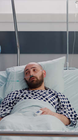 Practitioner nurse monitoring patient during sickness recovery writing disease symptom on clipboard working in hospital ward. Hospitalized sick man having respiratory disorderの写真素材