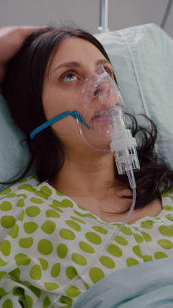 Close up of medical doctor putting oxigen mask to sick woman while resting in bed having respiratory emergency in hospital ward. Practitioner monitoring heart pulse checking sickness conditionの写真素材