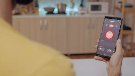 Man sitting in house with automation light system holding smartphone turning on light, controlling room ambiance with smart home application. Mobile with high tech app monitoring electricity effiencyの写真素材