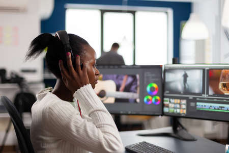 African video editor with headset listening music wihile editing footage and sound sitting in...