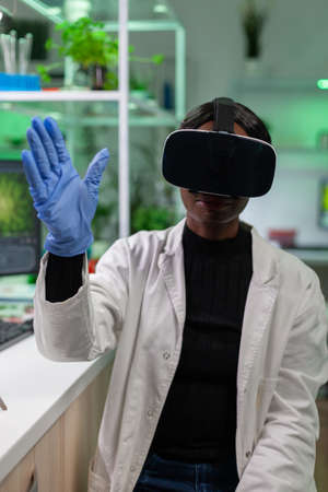 African scientist biologist conducting research using virtual reality wearing vr headset. Medical team working in pharmaceutical laboratory analyzing dna test.の写真素材