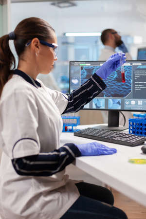 Medical researcher analyzing blood in test tube for vaccine development wearing protection glasses ....