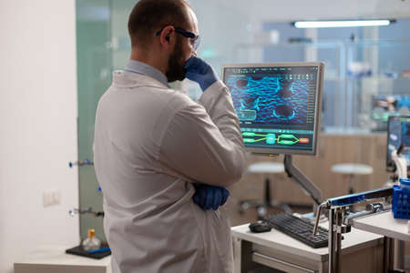 Scientist worried about virus evolution analysing DNA scan image standing, in equipped laboratory at computer. Stuff examining vaccine development using high tech researching treatment.の写真素材