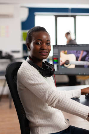African video editor looking at camera smiling editing video project in post production software...