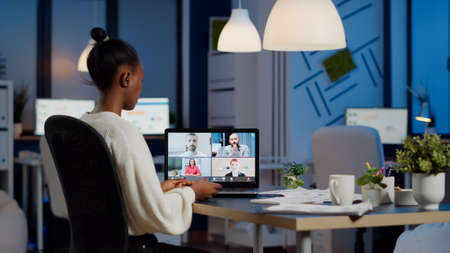 African employee working overtime from business office late at night discussing with partners online using webcam. Diverse team talking during corporate meeting using technology network wirelessの写真素材