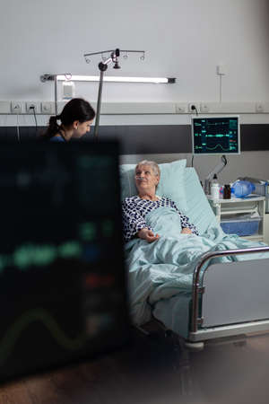 Medical nurse in scrubs showing compassion to senior woman patient, laying in hospital bed breathing...