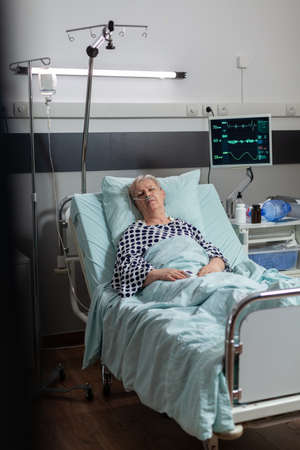 Elderly patient following recovery treatment laying in hospital bed, getting intravenous medicine...