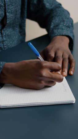 Close up of african american black person taking notes on notepad using a pen. Male adult hands of remote worker writing text on white paperの写真素材