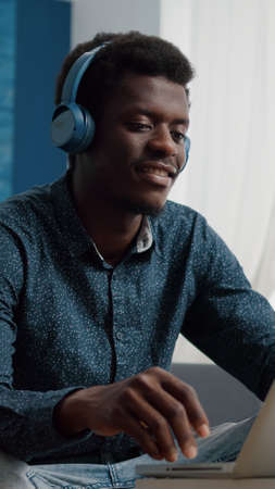 African american man with headphone on watching movie on streaming services in bright living room,...