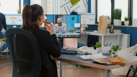 Executive manager eating pizza slice discussing with remote collegue during online videocall meeting conference. Takeout order food delivery in corporate place, meal break package delivered at office.の写真素材