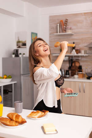 Woman singing during breakfast in home kitchen wearing sexy lingerie. Seductive woman with tattoos using smartphone wearing temping underwear in the morning.の写真素材